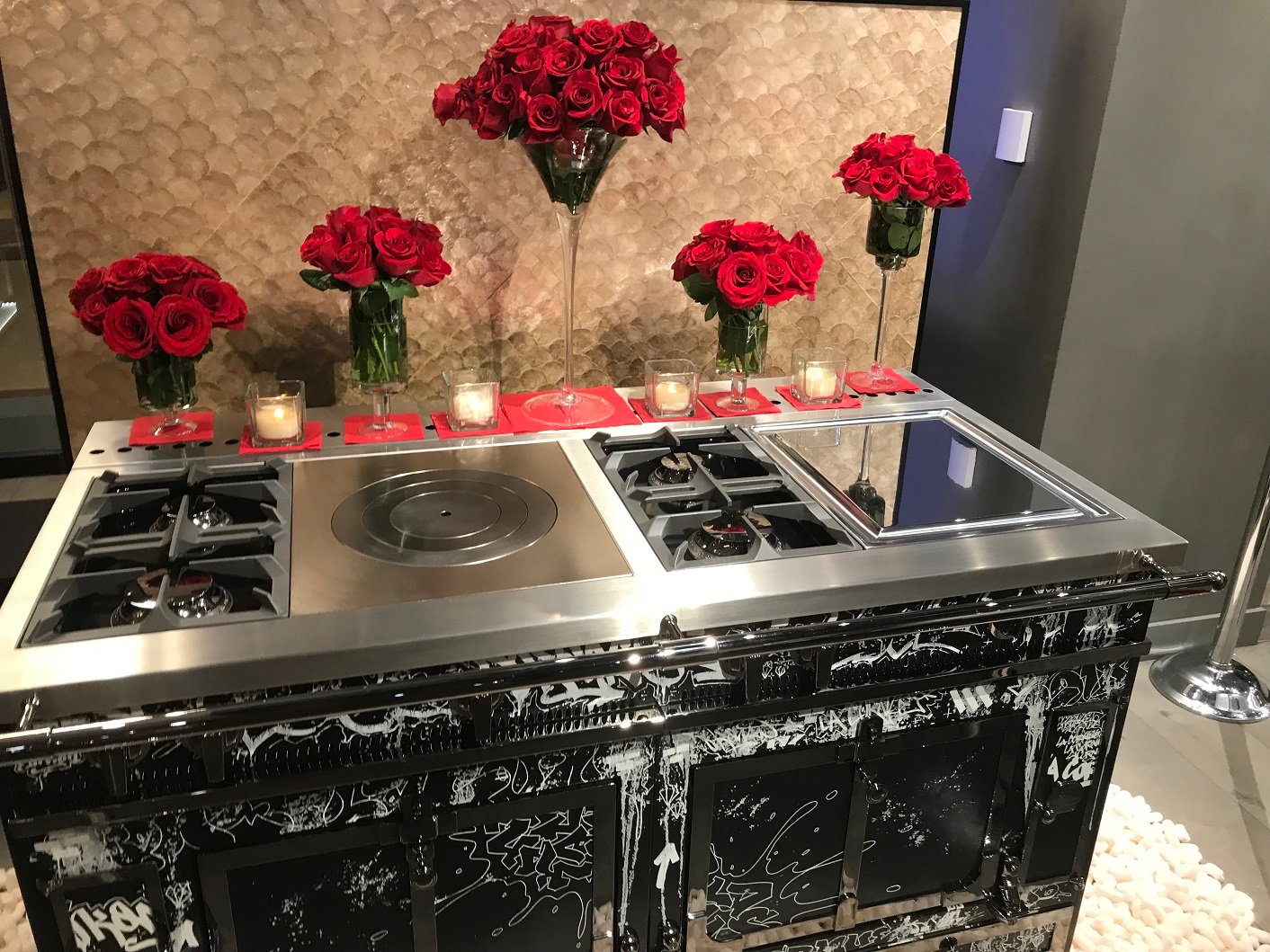 A stove with twin ovens in front of flower arrangements and with votive candles along the rear edge.