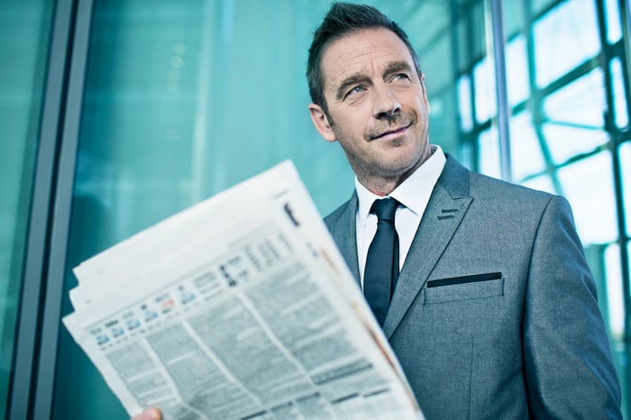 A smirking businessman reading a financial newspaper. 