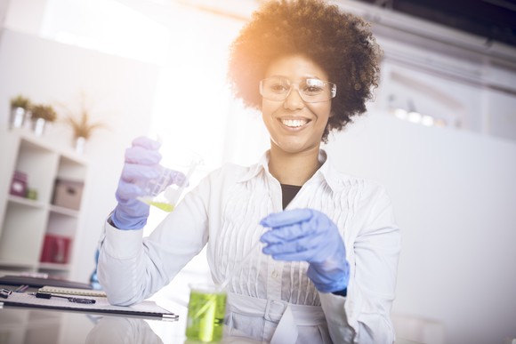 Smiling scientist holds beakers in a lab.
