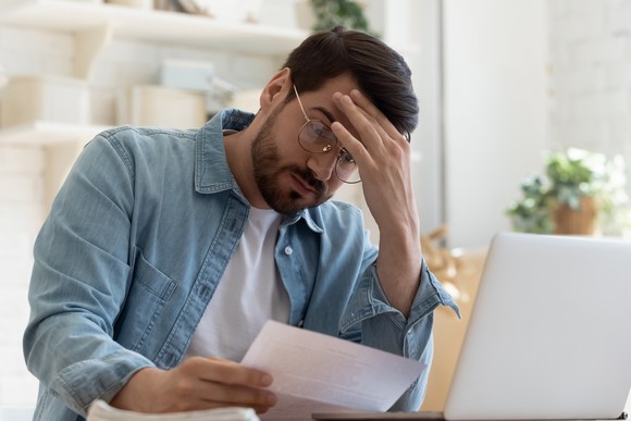 A man staring at a document with his hand on his forehead, expressing concern. 