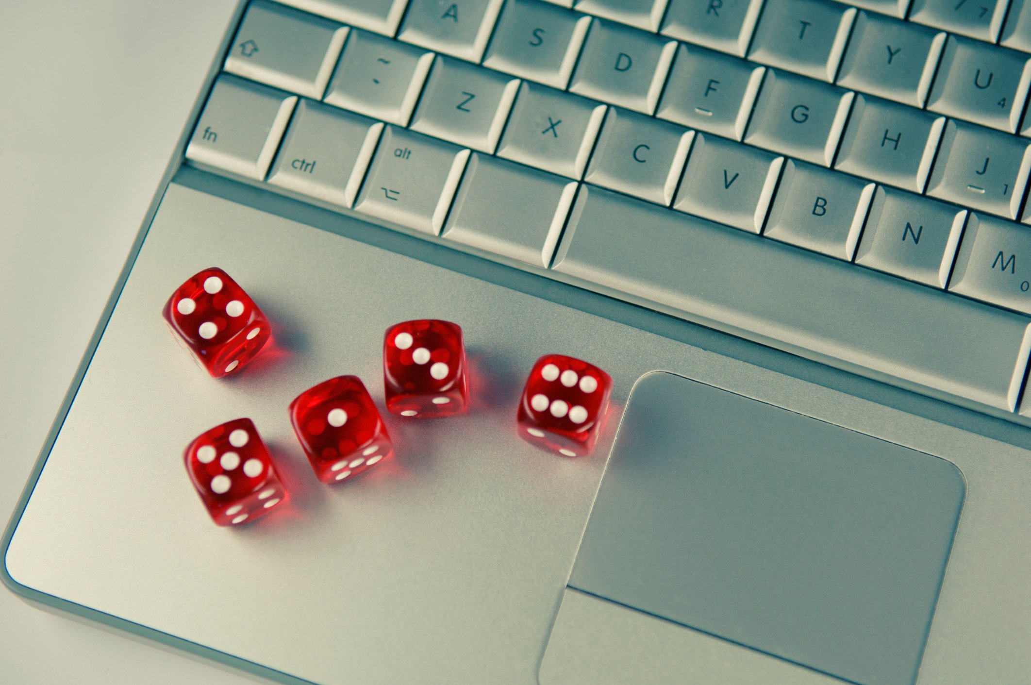 Five red dice on a silver laptop computer keyboard.