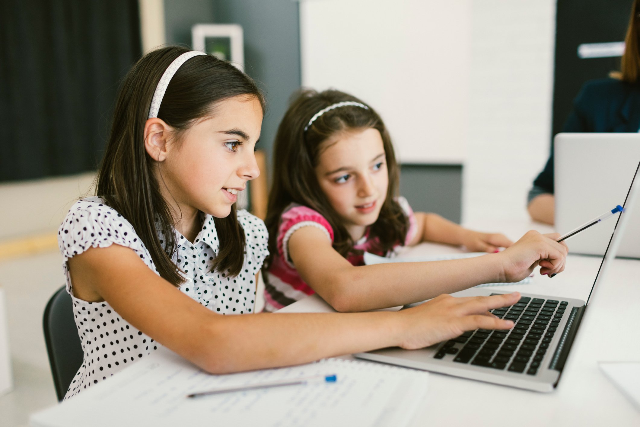 Two young girls work on a laptop.
