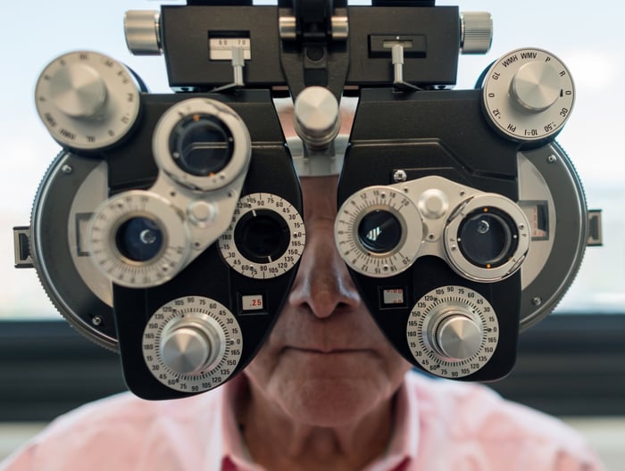 A man sits behind an opthalmologist's phoropter tool during an eye exam.