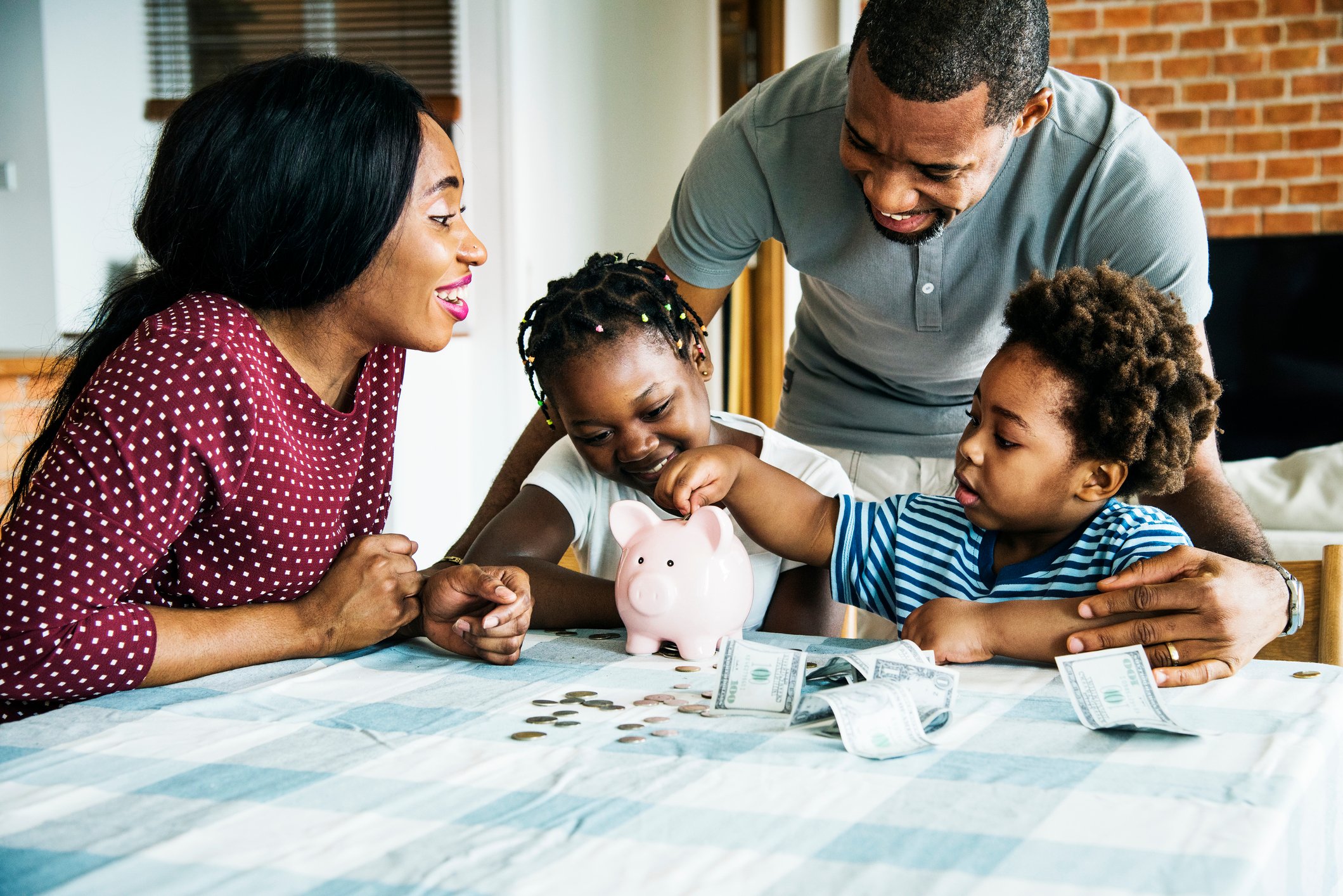 Two children put money in a piggy bank while two adults watch.