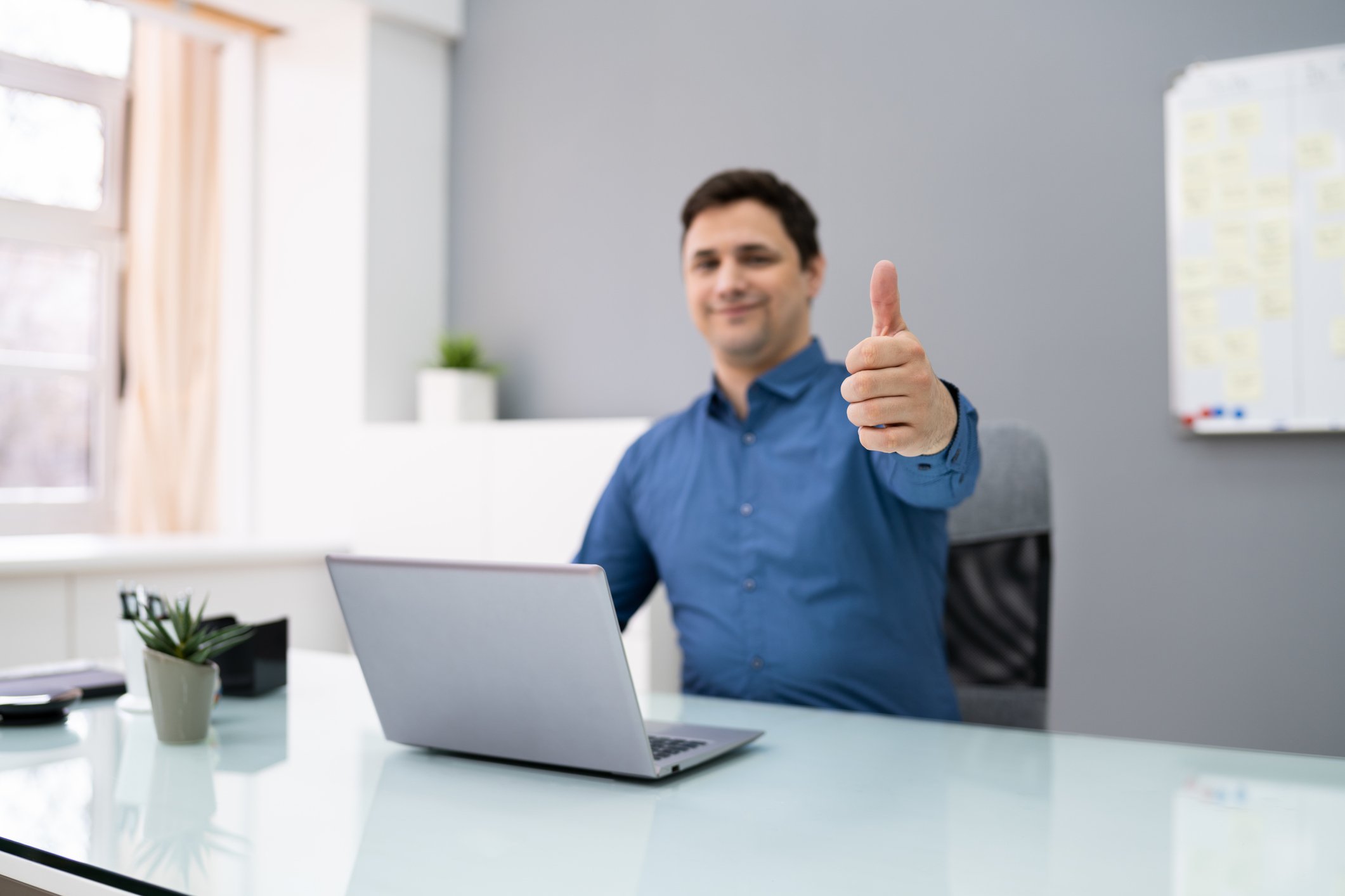 A person is sitting behind a computer and giving a thumbs-up.
