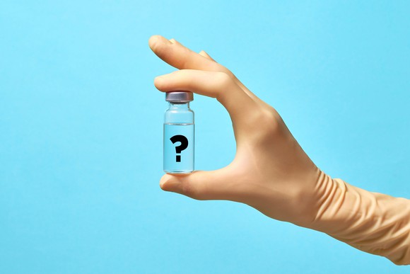 Gloved hand holding a vaccine vial with a question mark on it