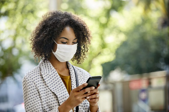 A woman wearing a mask and looking at her phone. 