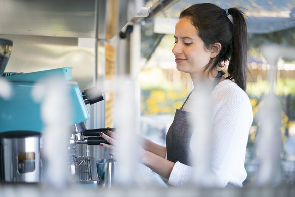 Lady barista smiling while preparing a cup of coffee at a coffee machine