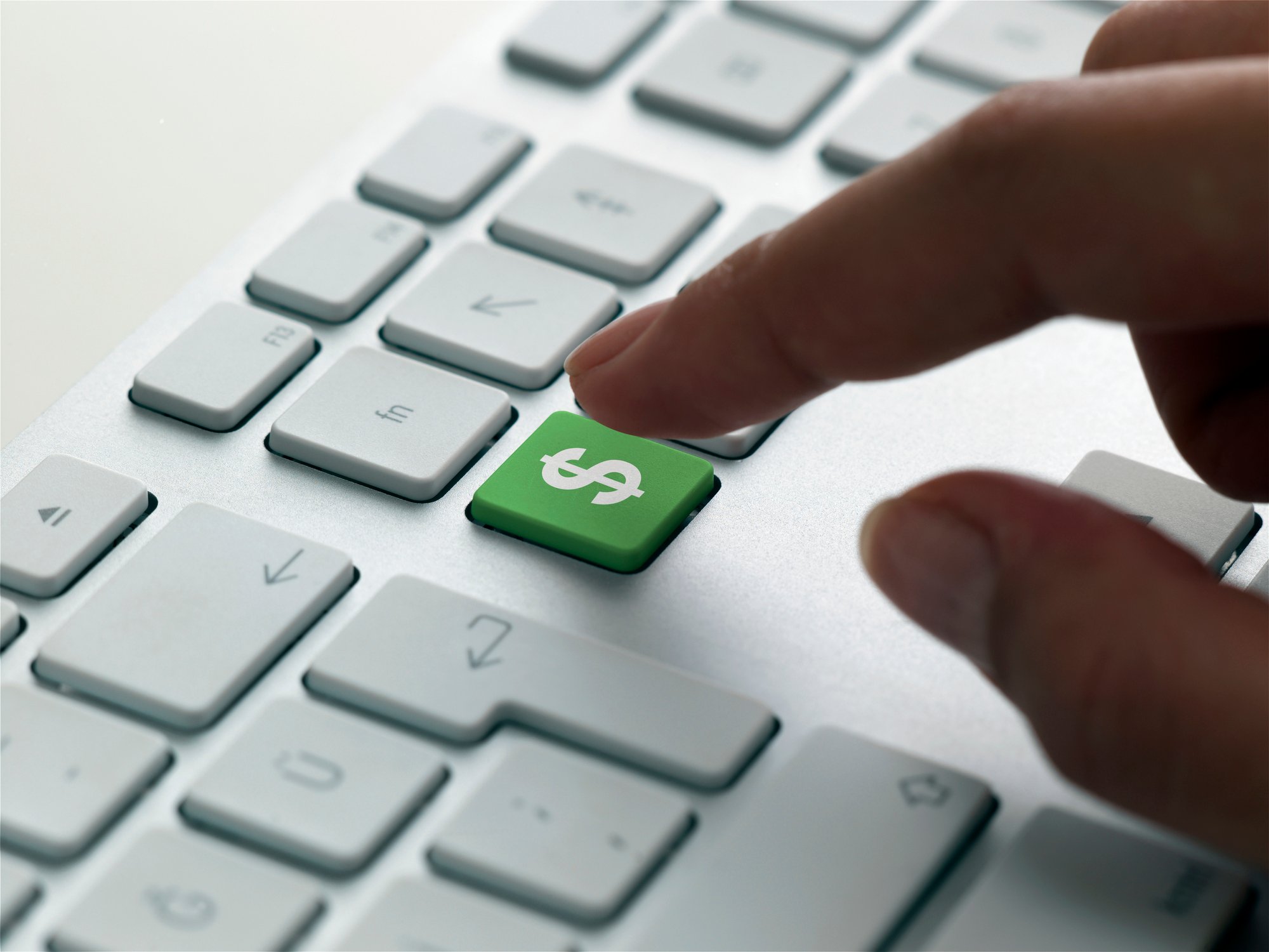 An investor's hand hovers over a green dollar sign on a computer keyboard. 