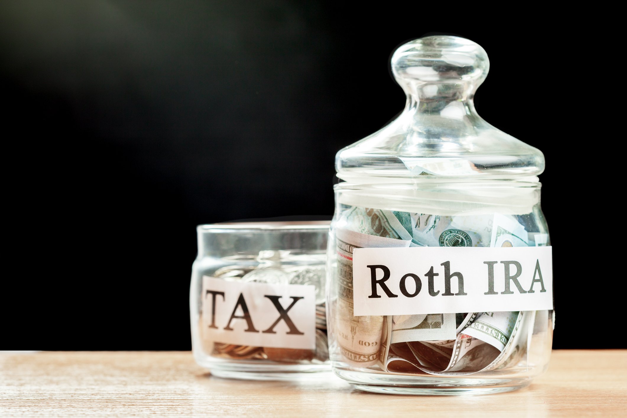Roth IRA money jar next to a small tax money jar. 