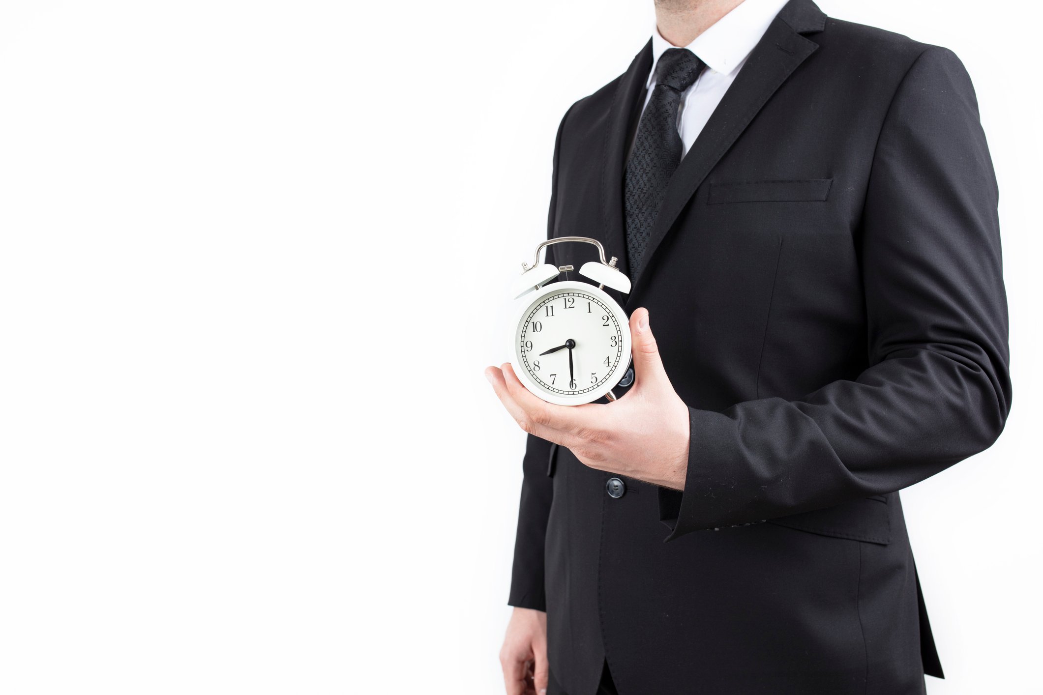 A businessman holds an alarm clock in one hand.
