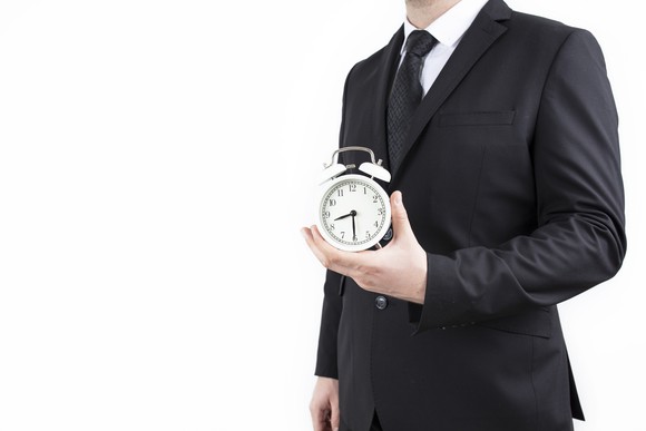 A businessman holds an alarm clock in one hand.