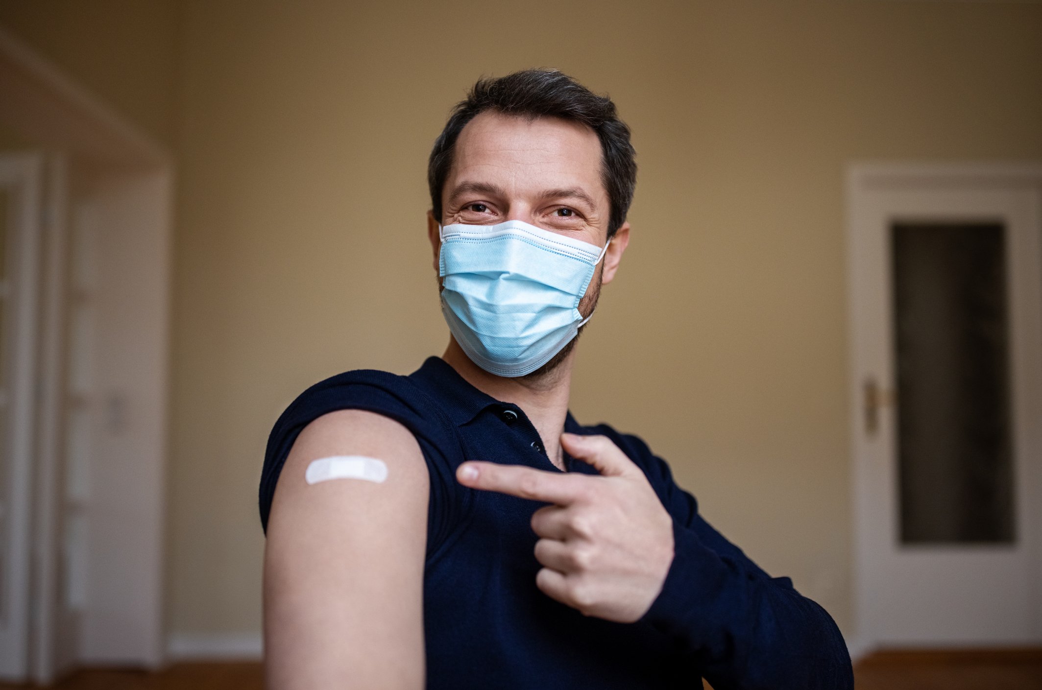 Man pointing to bandage over vaccination spot.