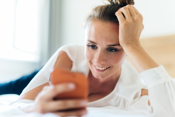 Woman lying on bed looking at phone and smiling