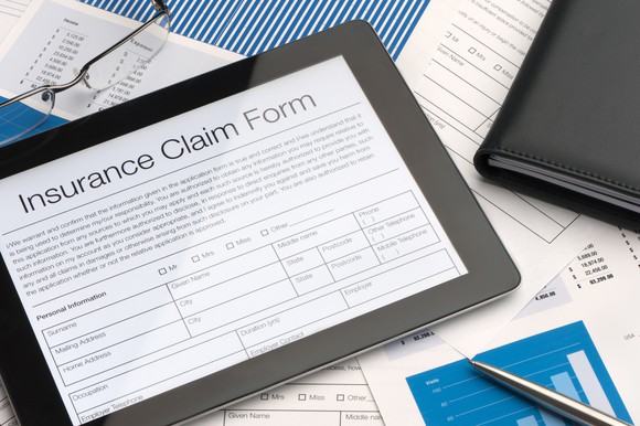 A tablet with an digital insurance claim form sits on a pile of paperwork