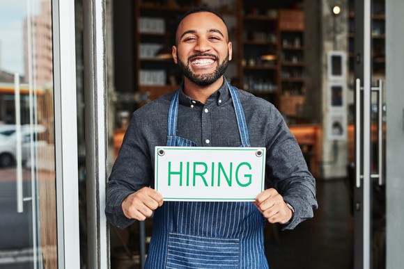 A shop owner holding a "hiring" sign.