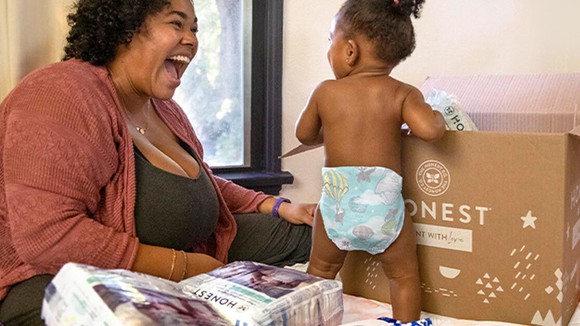 A woman smiling at a baby leaning against an Honest Company box. 
