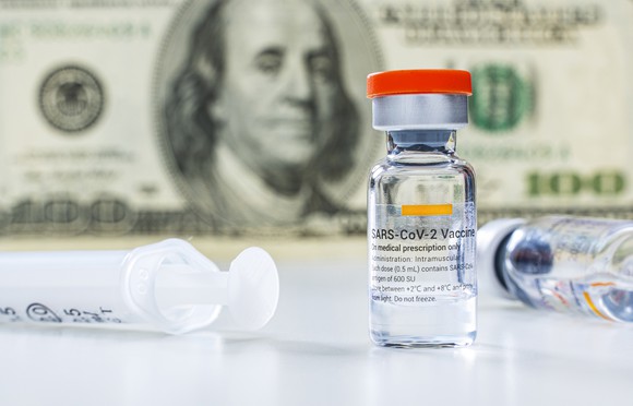 Vials of coronavirus vaccine and syringe next to hundred dollar bill.