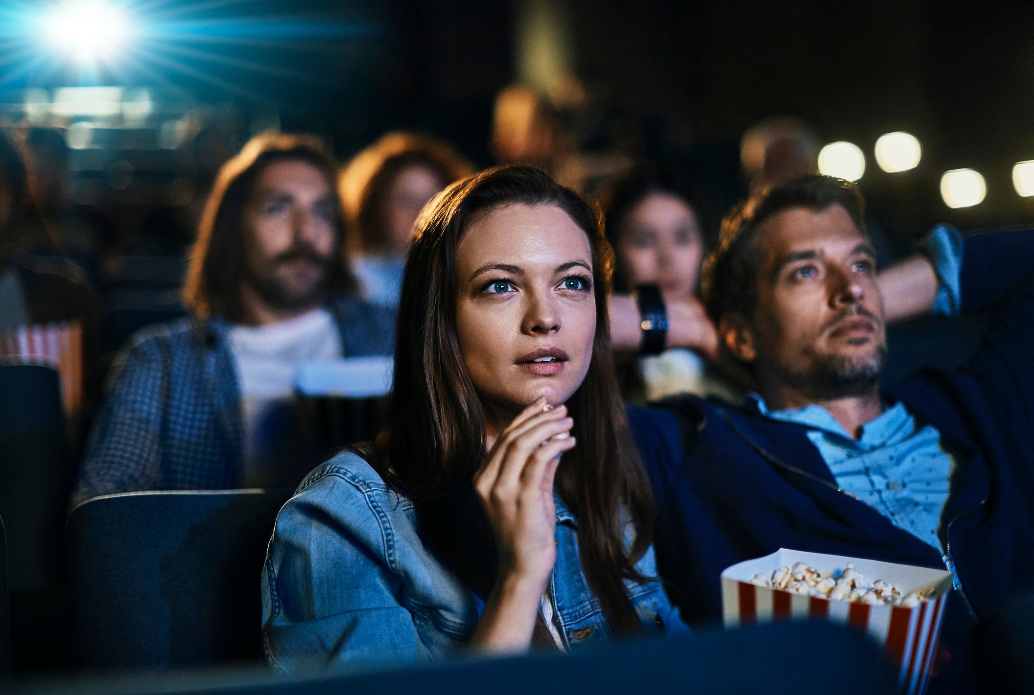A couple eating popcorn while watching a movie at a crowded theater. 