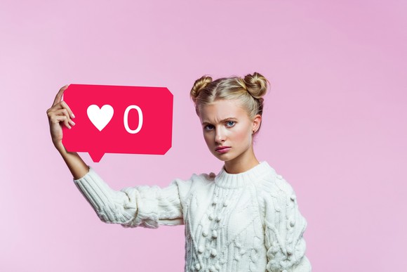 An upset teenage holding a sign showing zero likes.