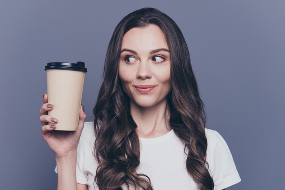 A young woman holding a to-go coffee cup.