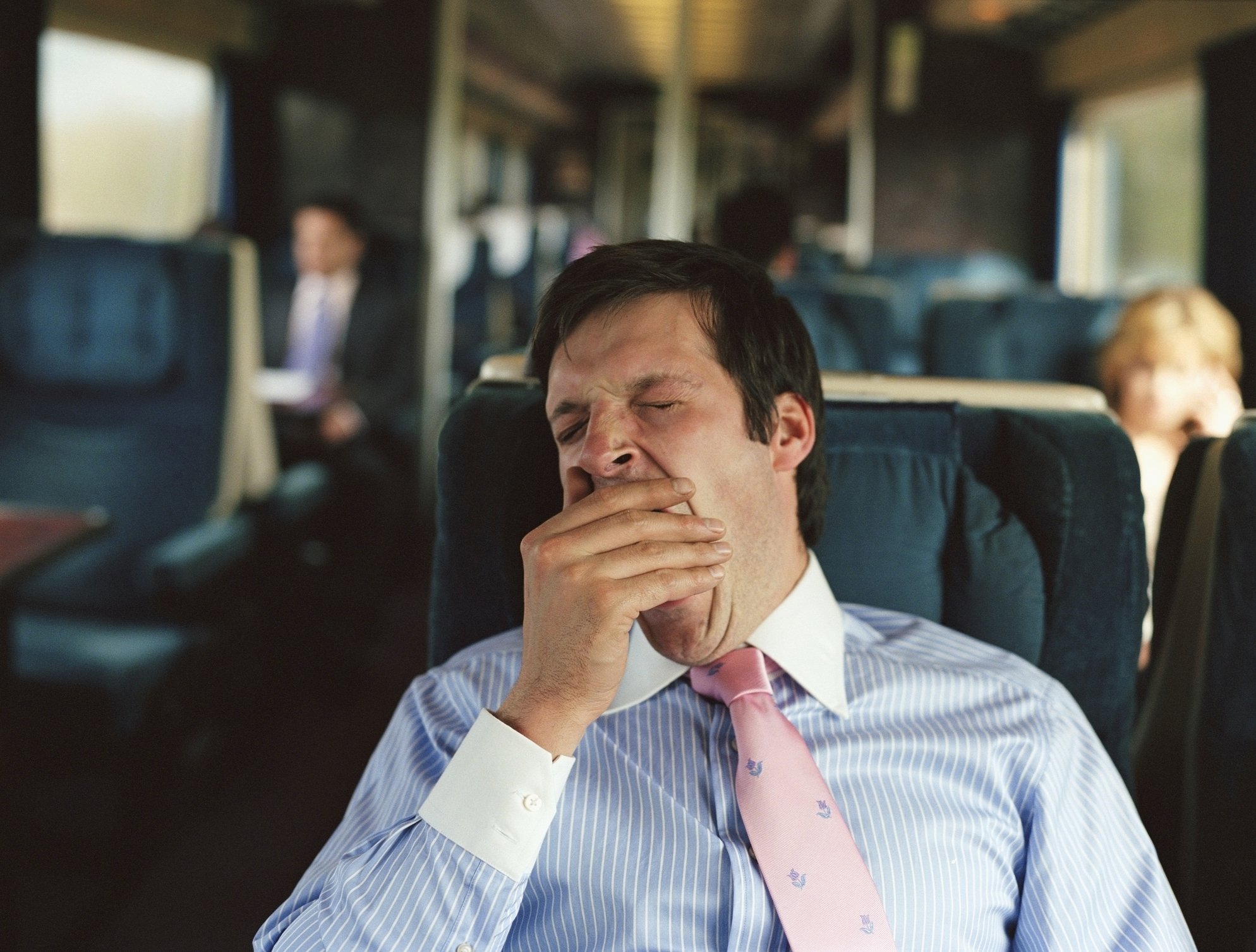 A businessman yawns while sitting in a seat on a train.