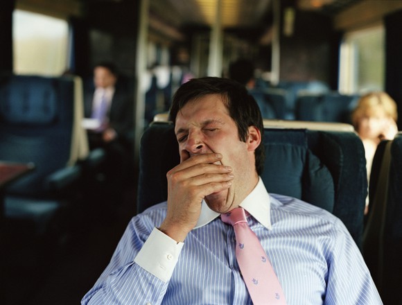 A businessman yawns while sitting in a seat on a train.