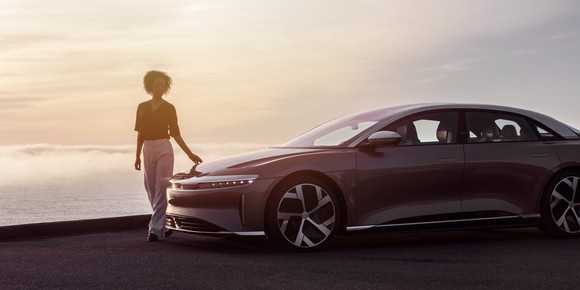 A woman standing next to a Lucid Air sedan