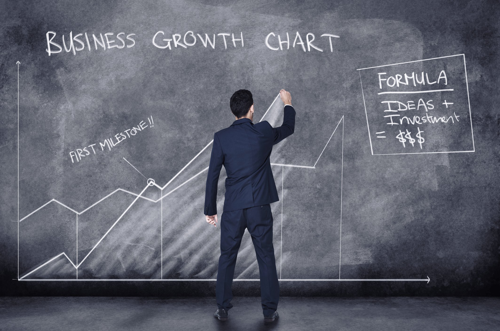 A man drawing on a large chalkboard that says business growth chart. 