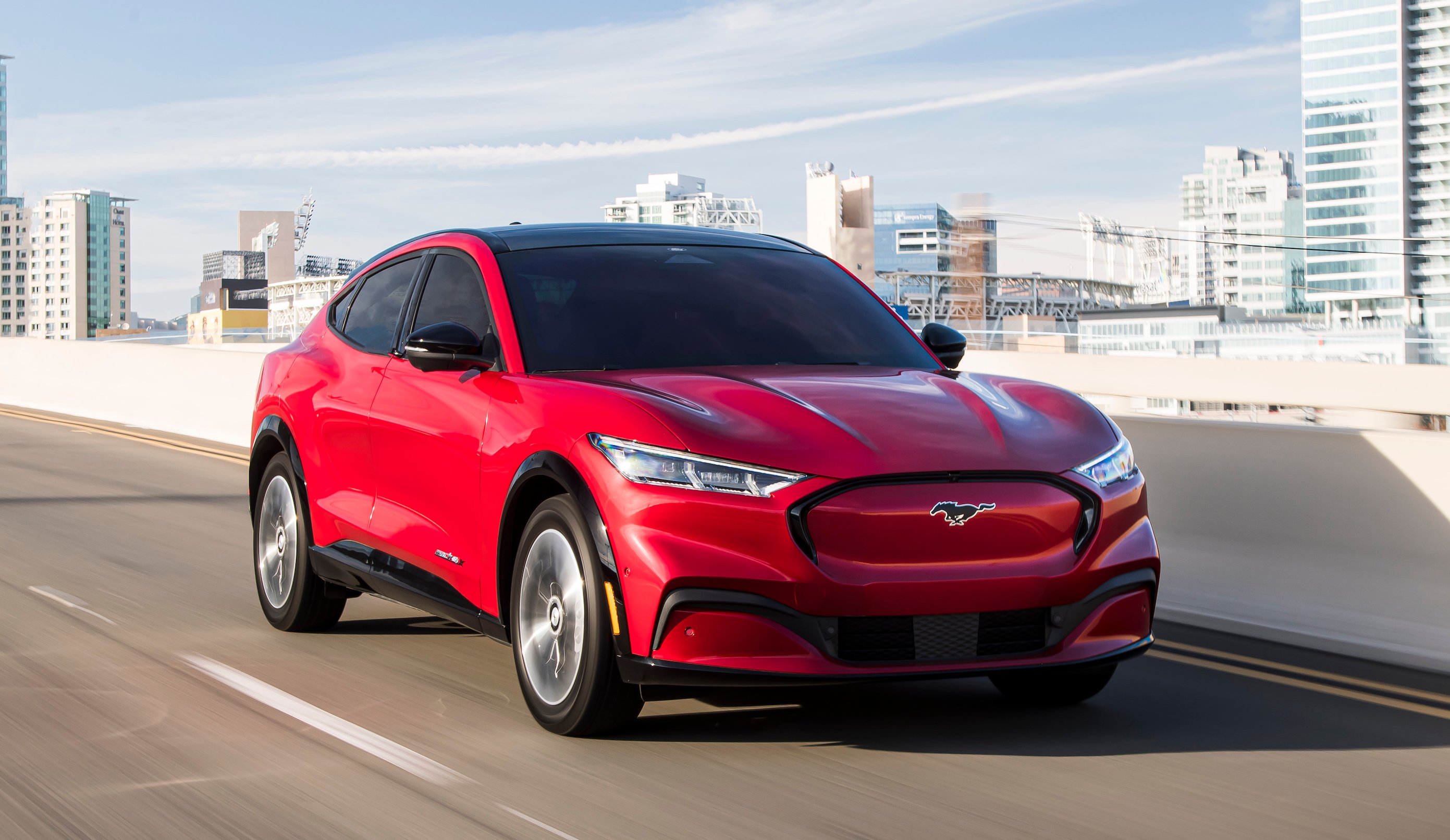 A red Ford Mustang Mach-E, a sporty electric crossover SUV, on a city highway