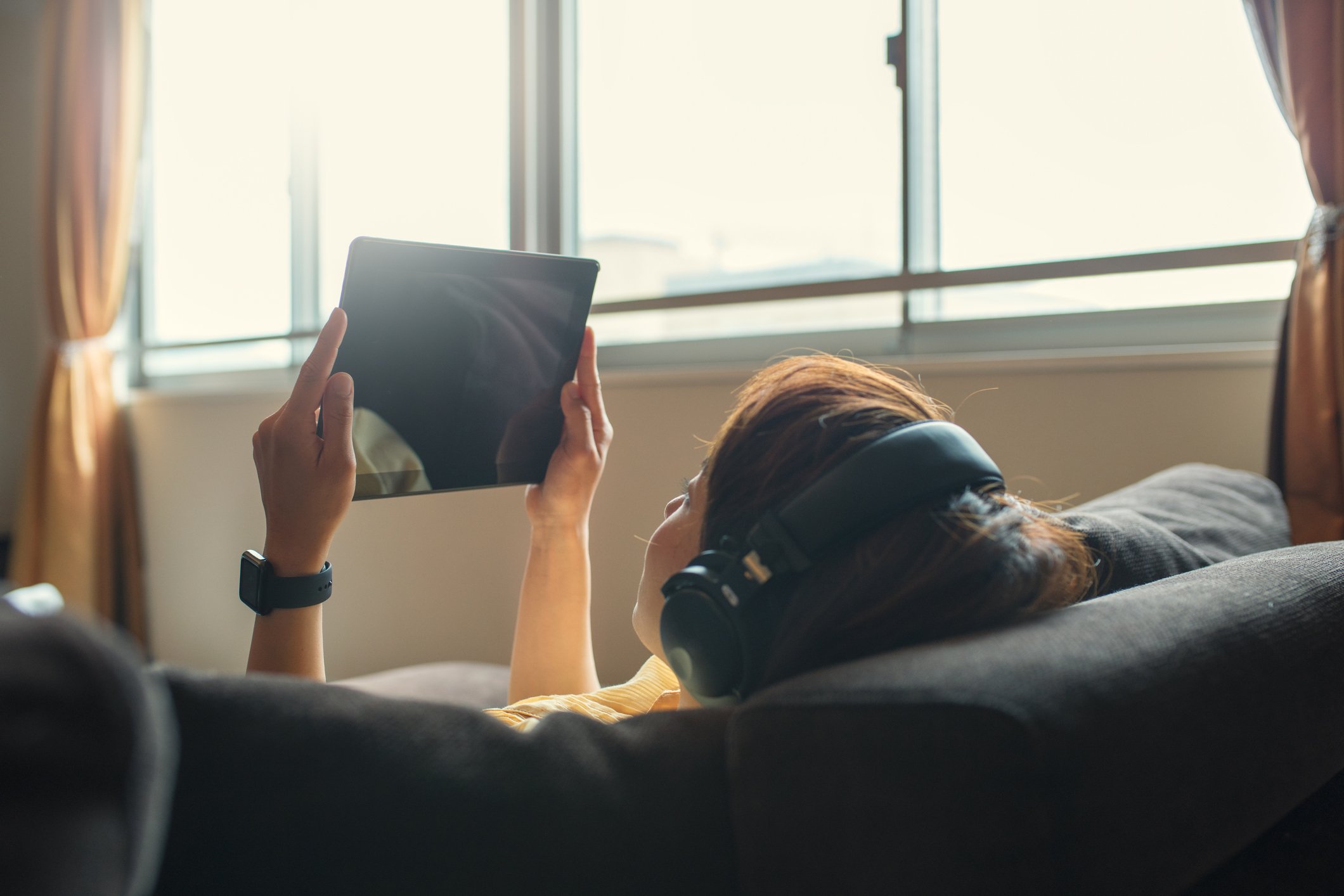 A woman watching streaming content on a tablet while reclining on a couch.