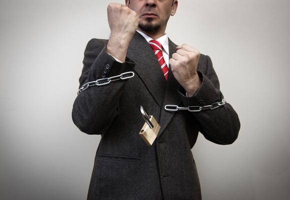 A businessman with fists raised is breaking free of chains.