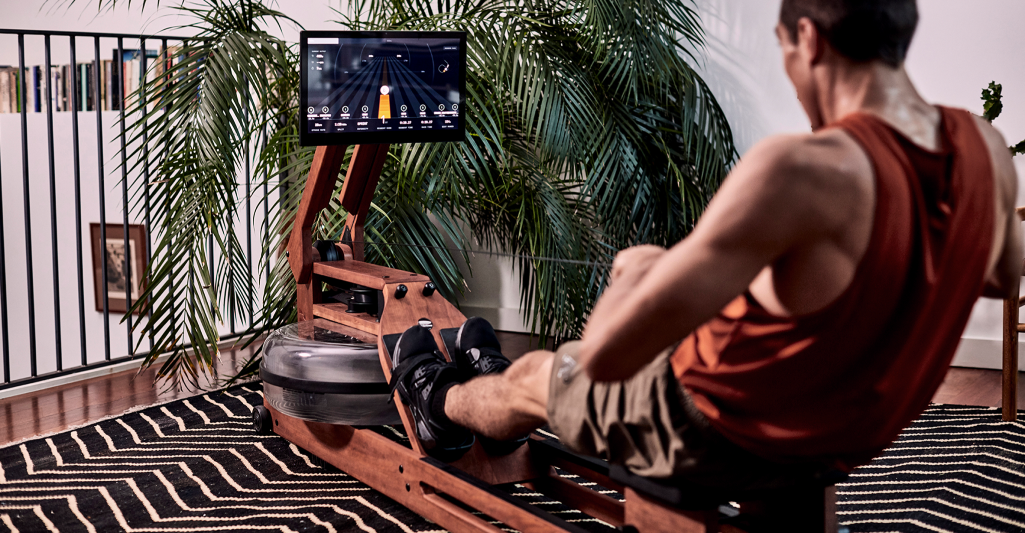 A man using an Ergatta rowing machine while playing a competitive workout game against 7 other users.