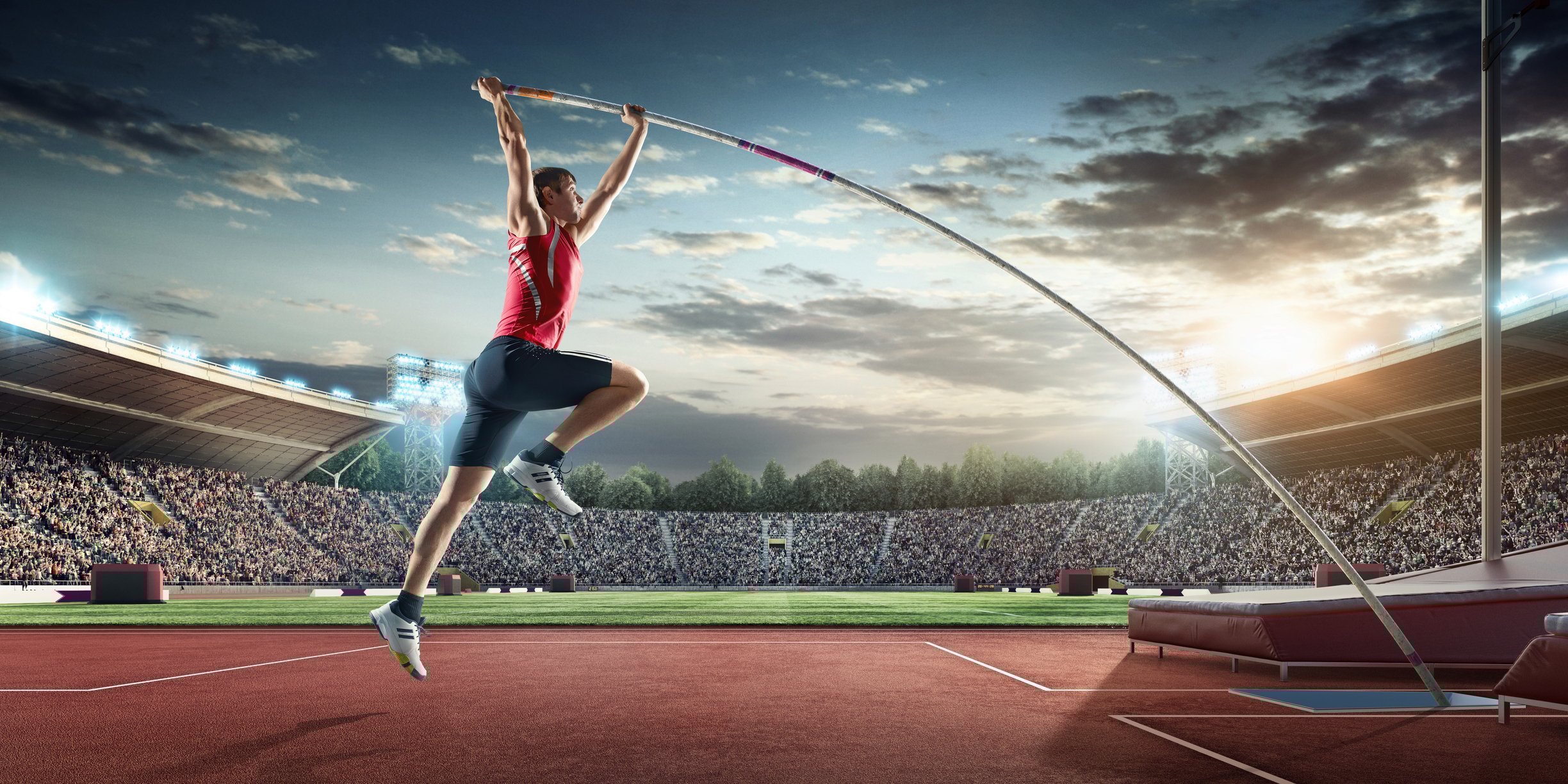 A man pole-vaults in front of a crowd in a stadium.  
