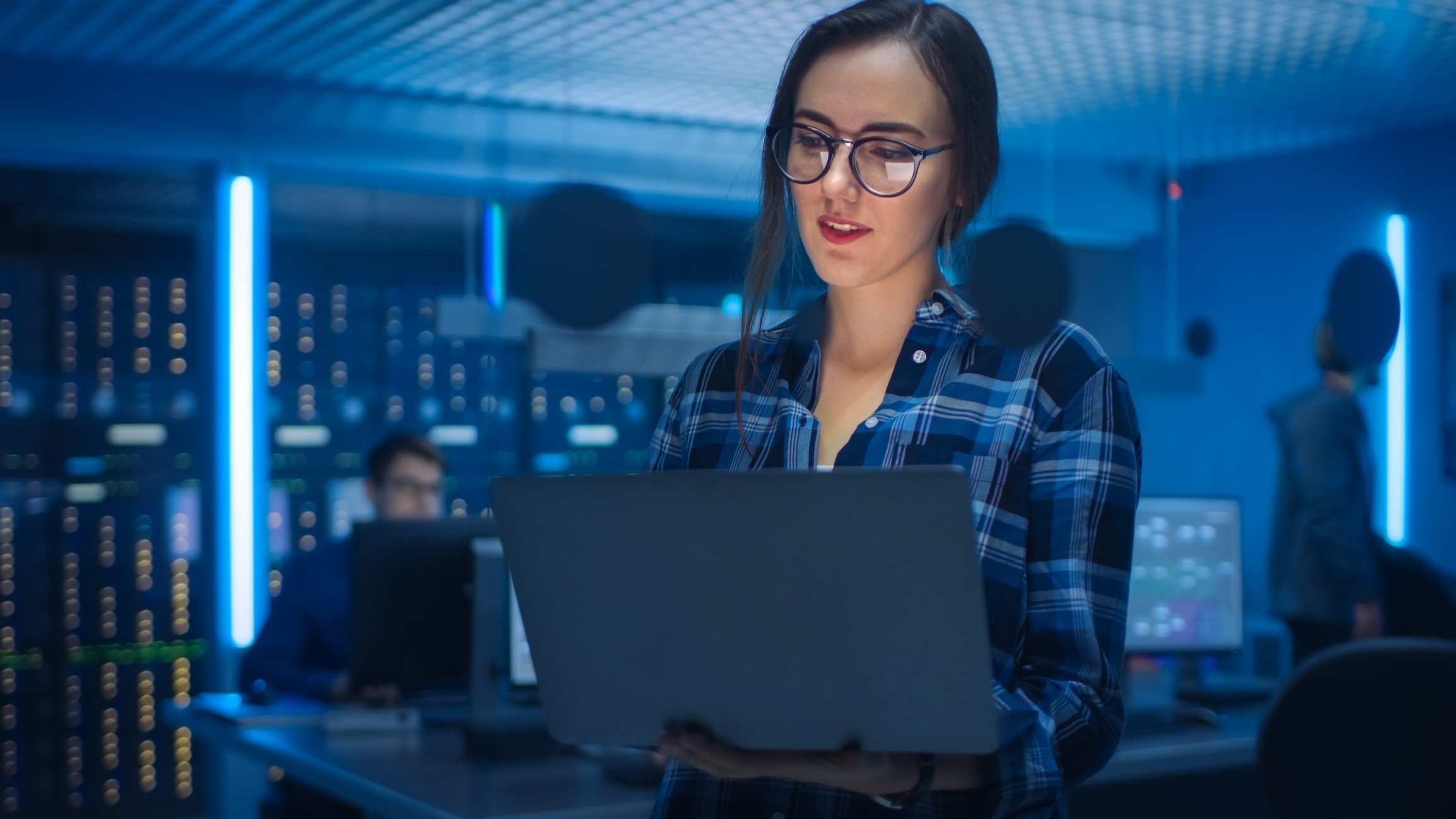A woman works at her laptop in a darkened room filled with servers.