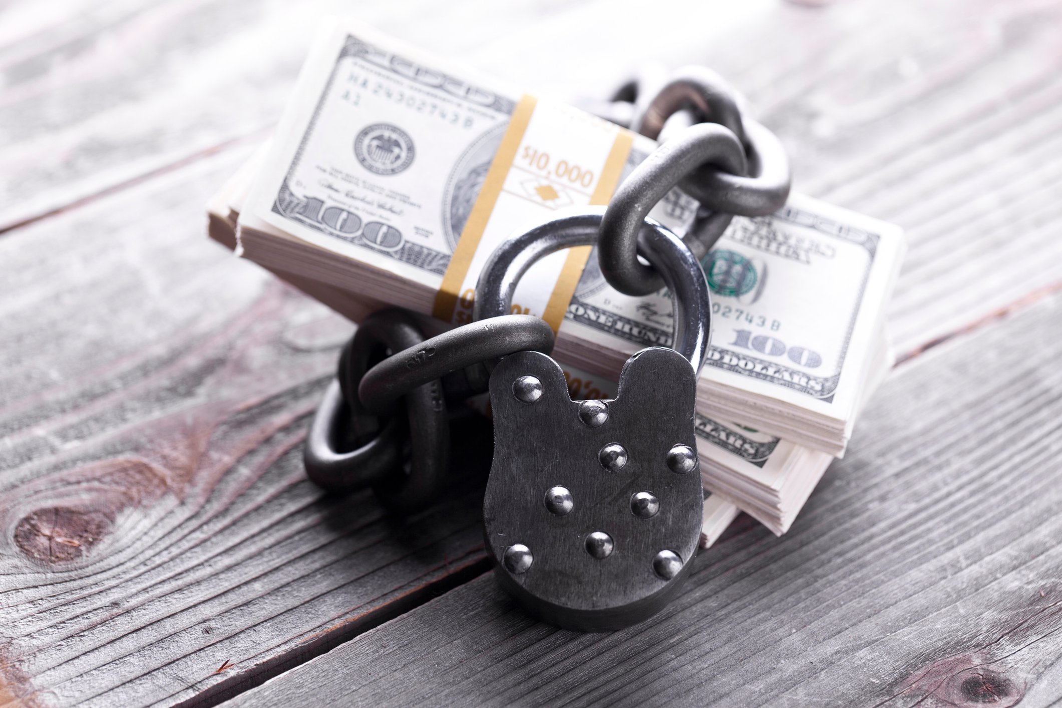 A chain and lock wrapped around a stock of money, sitting on wooden 2x4s.