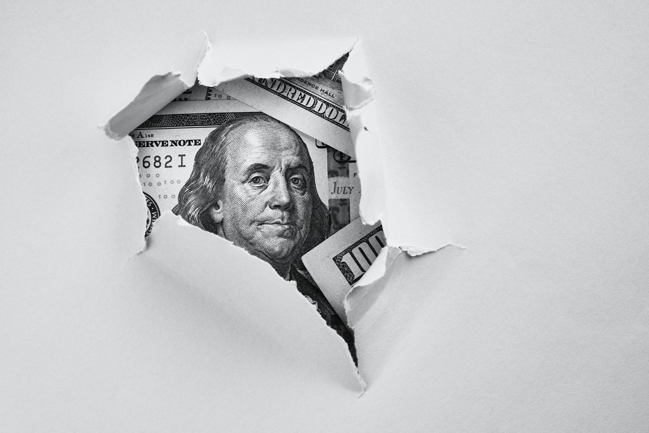 A sheet of paper with a torn hole revealing a hundred dollar bill.