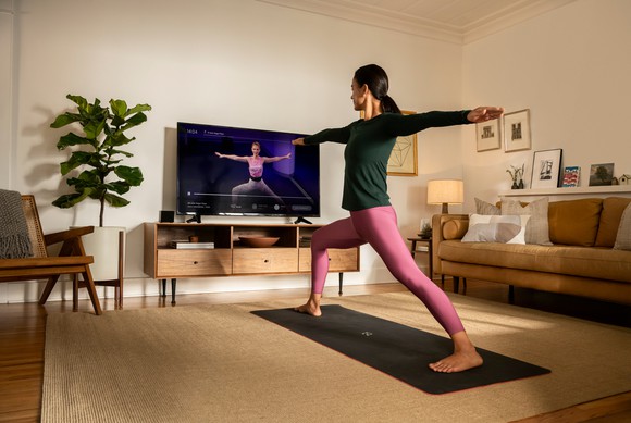 A person does yoga at home while watching video content from Peloton on TV.