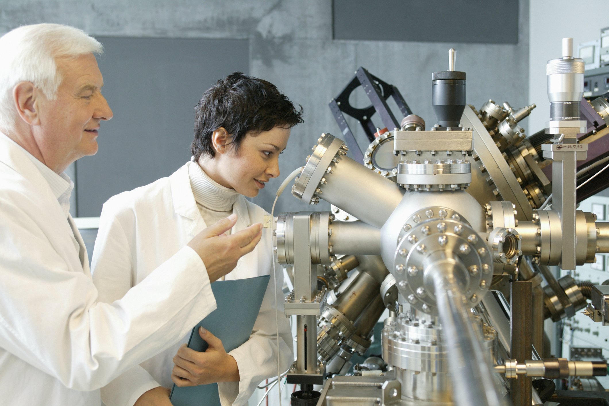 Two people observe manufacturing equipment.
