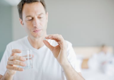 man holds pill and glass of water