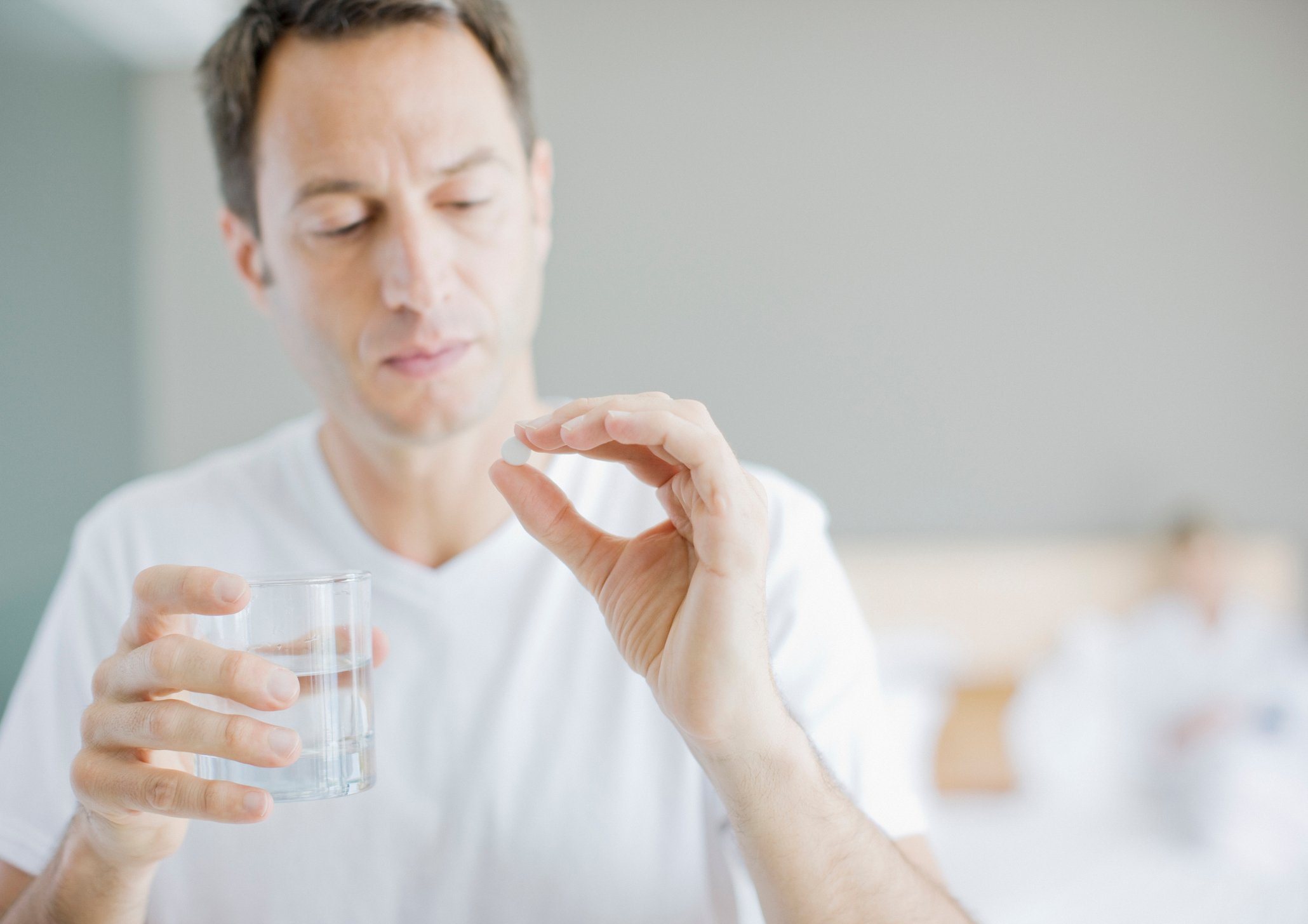 Person holds glass of water in one hand and a white pill in the other.