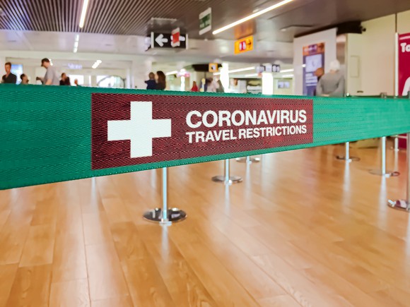 A barrier with a sign saying Coronavirus Travel Restrictions in an airport