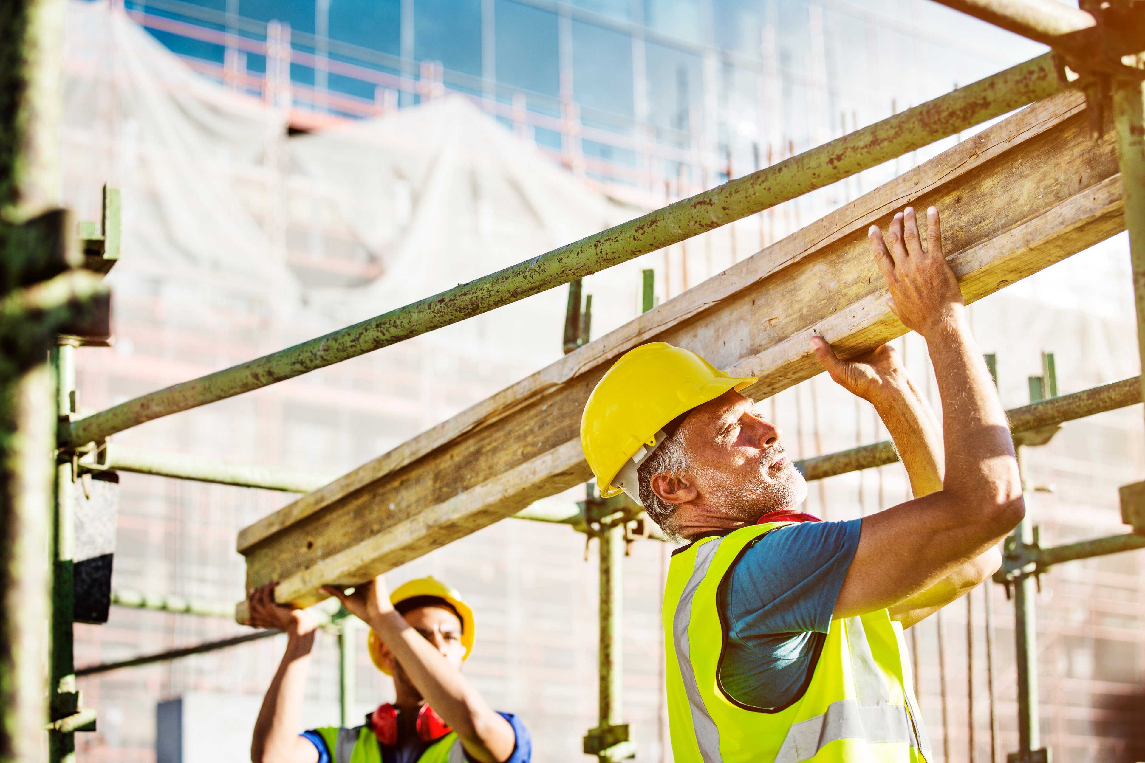 Two workers carry lumber on a construction site.