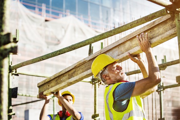Two workers carry lumber on a construction site.