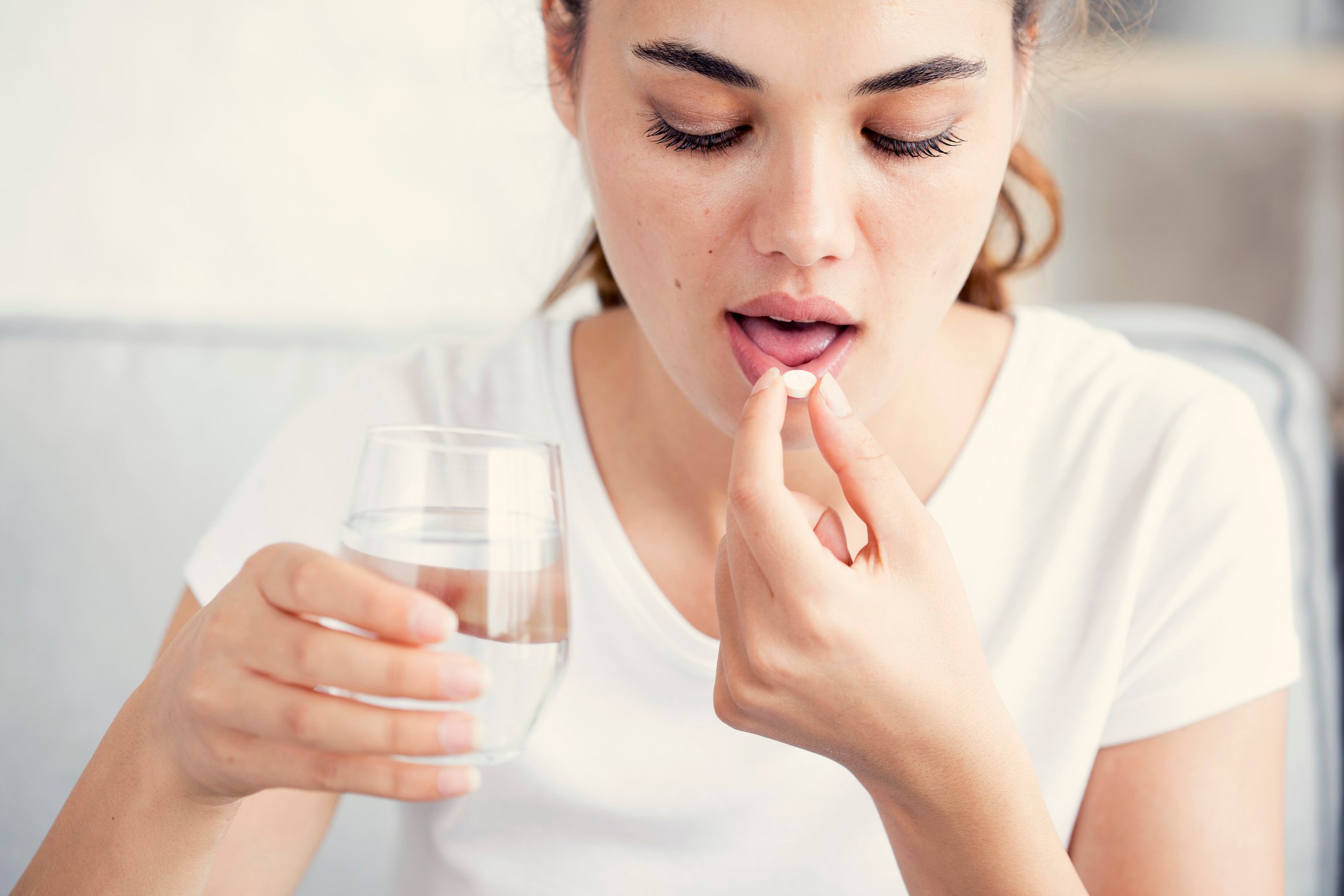A young woman takes a pill with a glass of water.