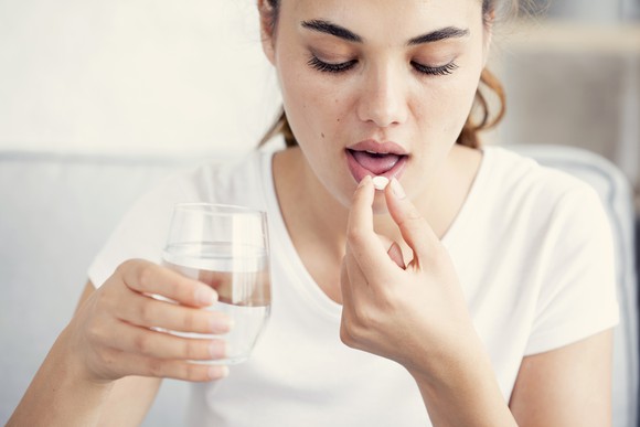 A young woman takes a pill with a glass of water.
