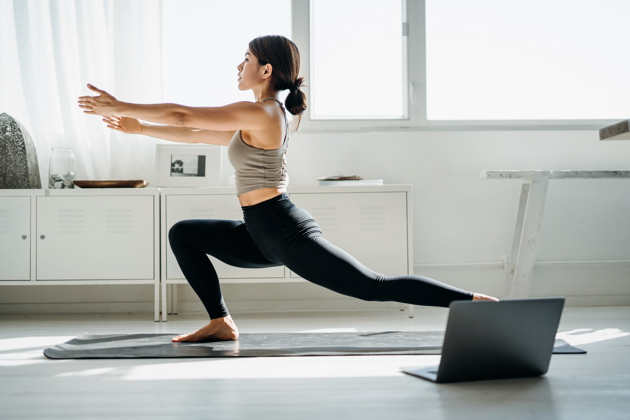 A woman does yoga in front of her laptop at home.