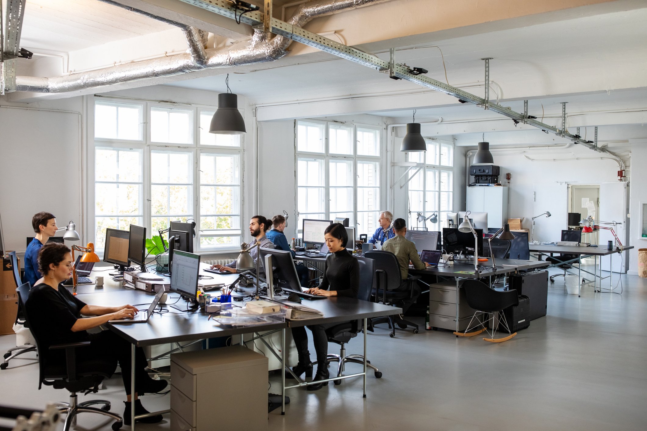 An industrial-style open concept office with many developers and engineers sitting at workstations.