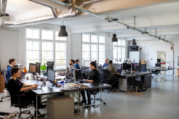 An industrial-style open concept office with many developers and engineers sitting at workstations.