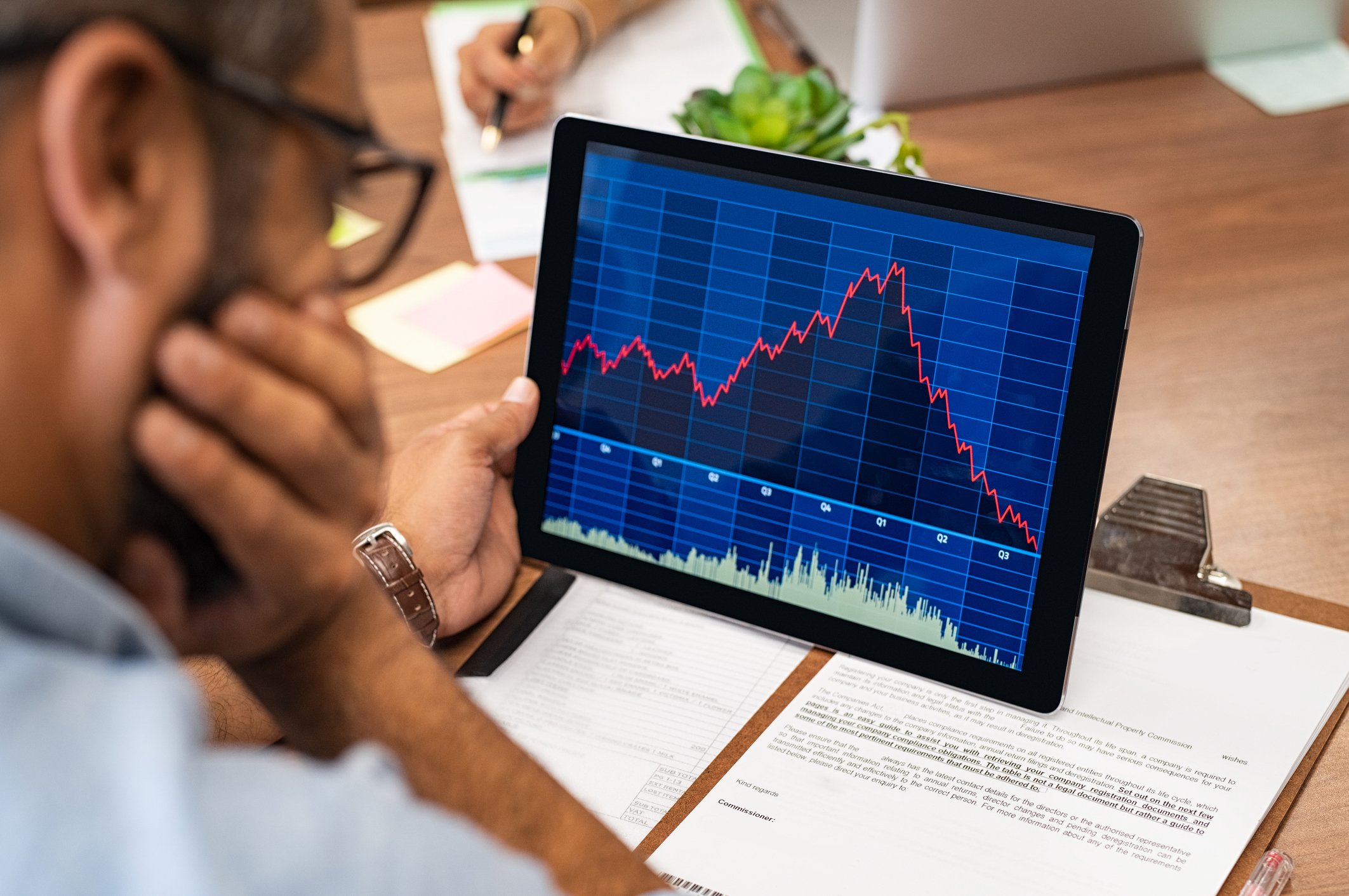 A man looking at a screen with a stock chart going up and then down.